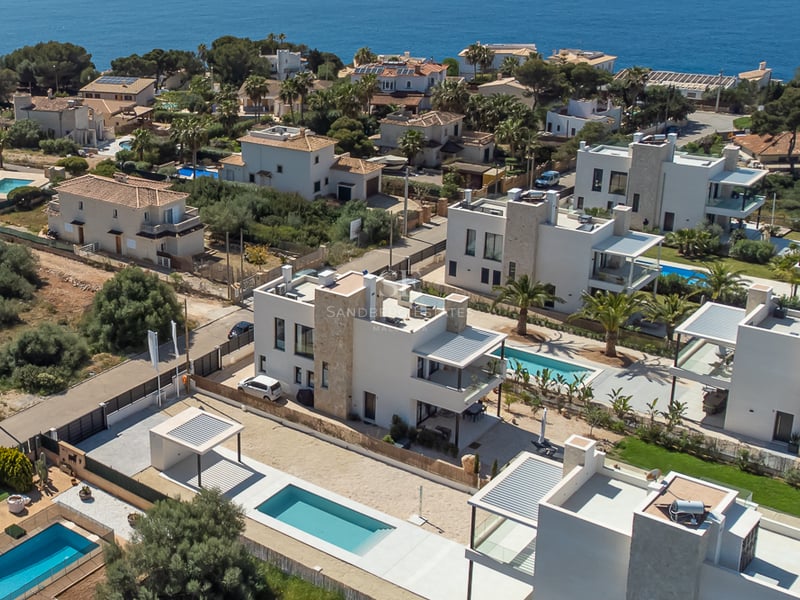 Vue par drone de villas blanches modernes avec piscines privées et accents de pierre dans un quartier côtier méditerranéen.