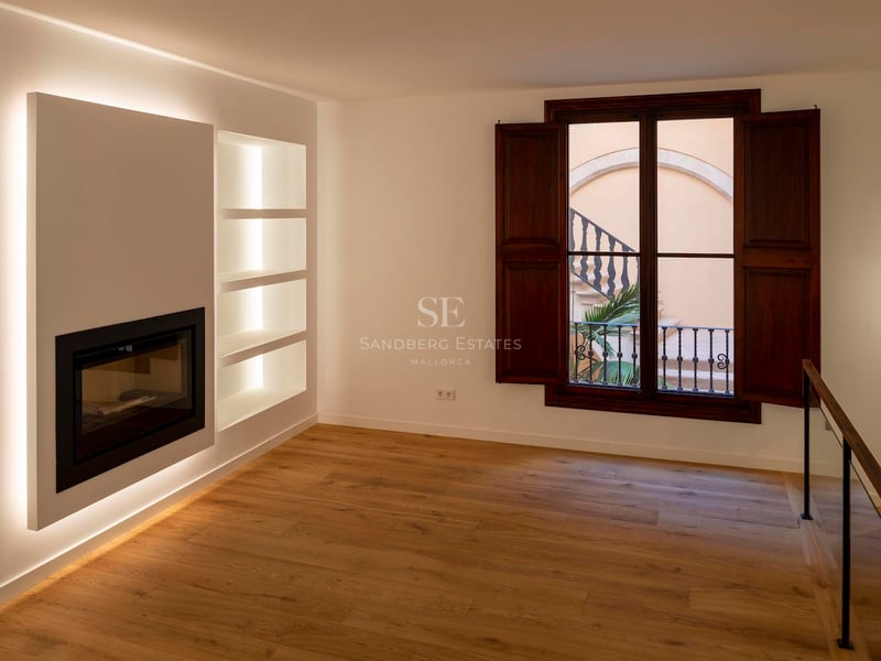 Pièce moderne vide avec cheminée intégrée, étagères rétroéclairées, parquet en chêne et volets en bois foncé.
