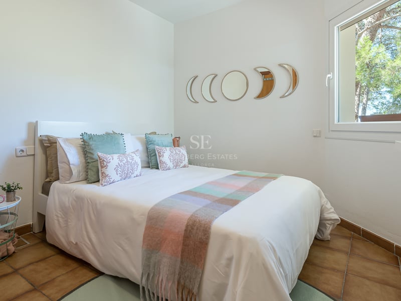 Chambre avec lit blanc, sol en terre cuite et miroirs phases de lune au-dessus de la tête de lit.
