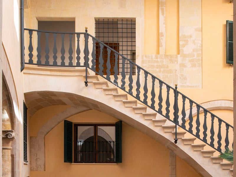 Cour intérieure avec un escalier en pierre, des rampes en fer forgé et des murs ocre chaleureux.