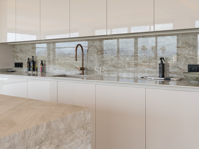 Cuisine contemporaine avec placards crème sans poignées, crédence en marbre veiné et robinetterie design en bronze.