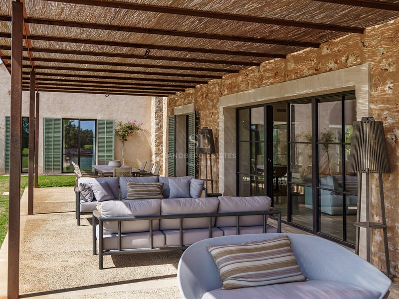 Zona de estar exterior techada con sofás modernos, pared de piedra rústica y techo de vigas de madera.