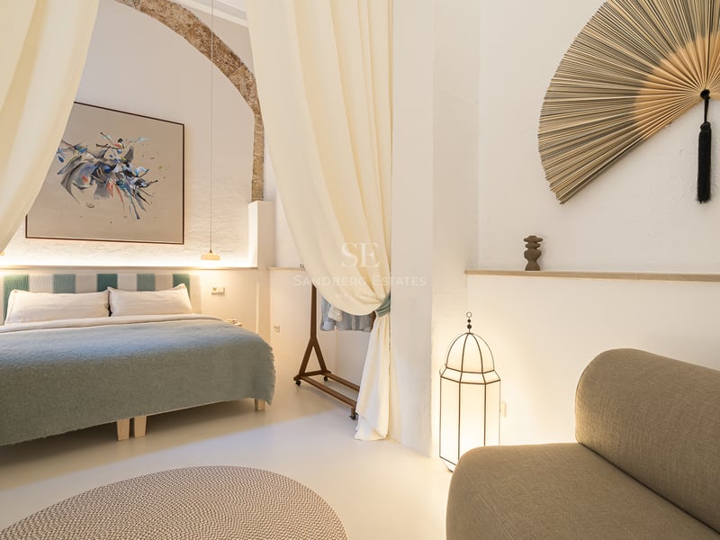 Chambre élégante avec grand lit, rideaux fluides, arche en pierre et décoration artistique.