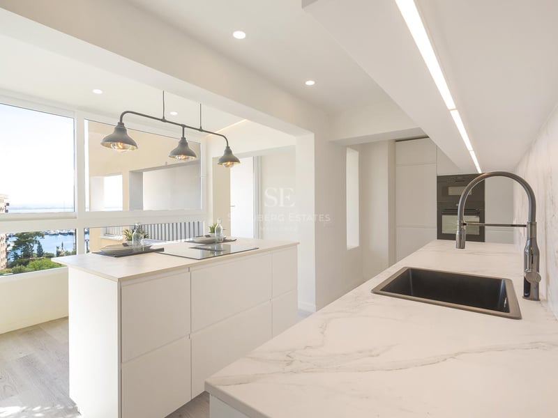Cuisine moderne lumineuse avec îlot blanc, plans de travail en marbre et fenêtre donnant sur un port de plaisance.