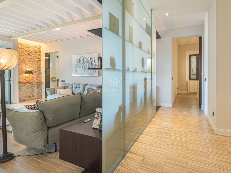 Salon avec canapé gris, parquet en bois, mur en pierre naturelle et cloison en verre dépoli.