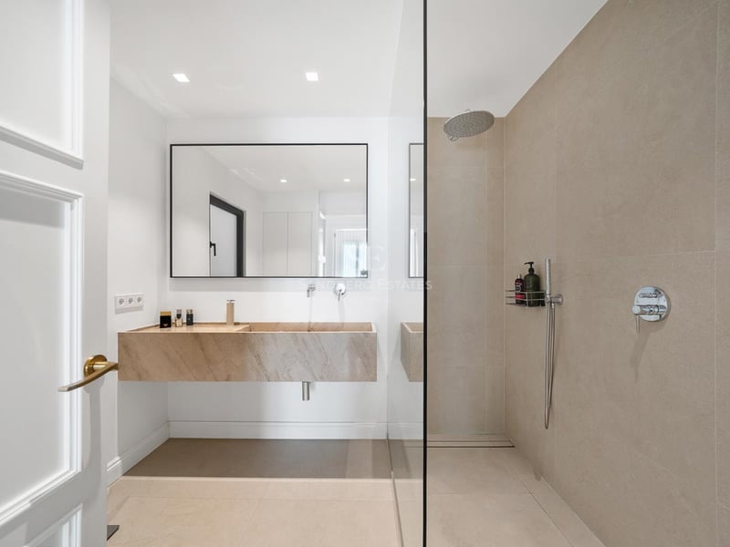 Salle de bain moderne avec vasque suspendue en pierre, grand miroir et douche à l'italienne.