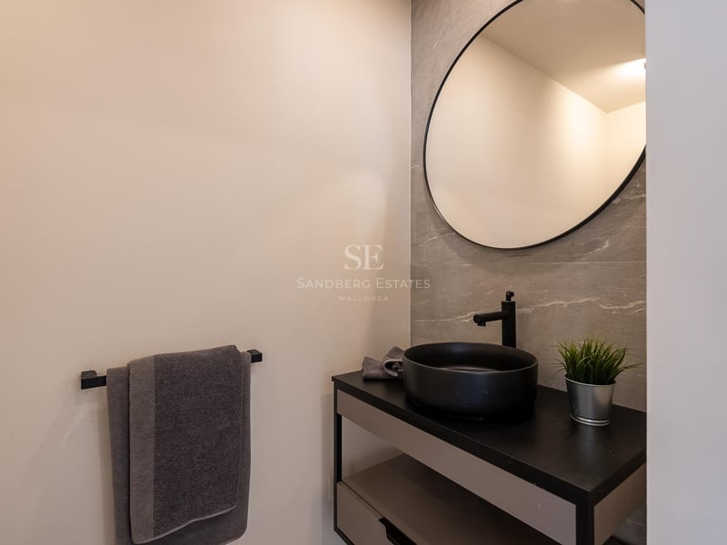 Salle de bains moderne avec miroir circulaire, vasque noire et carrelage mural effet pierre grise.