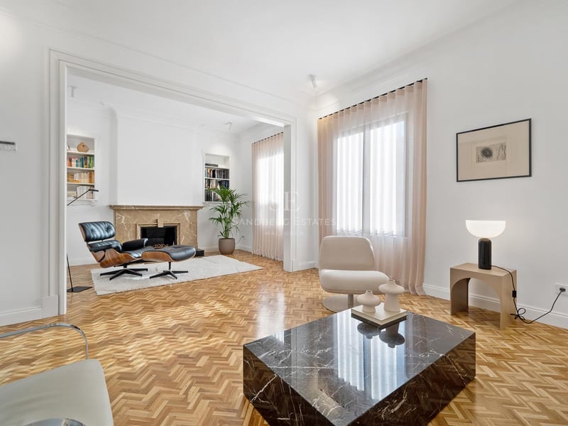 Salon lumineux avec parquet en chevrons, table basse en marbre noir et fauteuil Eames près d'une cheminée.