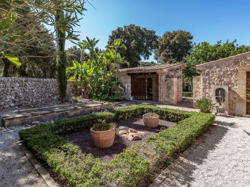 Jardin méditerranéen avec murs en pierre, allées de gravier et dépendances sous un ciel bleu clair.