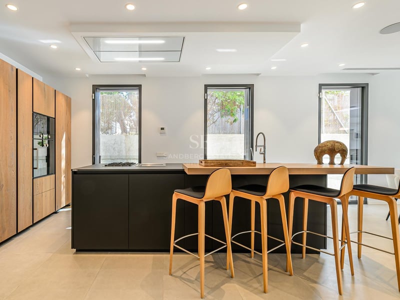 Cuisine moderne avec îlot noir, bar en bois, quatre tabourets et armoires en bois du sol au plafond.