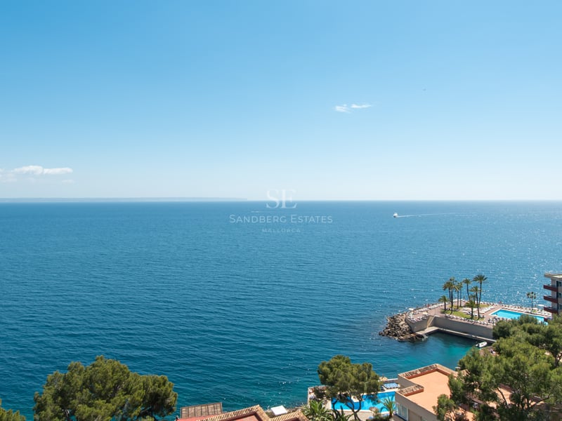 Vue en plongée sur la mer Méditerranée avec bâtiments côtiers et piscines sous un ciel bleu clair.