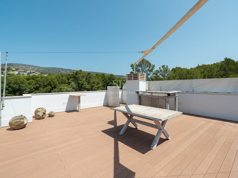 Grande terrasse sur le toit avec plancher en bois, murs blancs, table en bois et voile d'ombrage.
