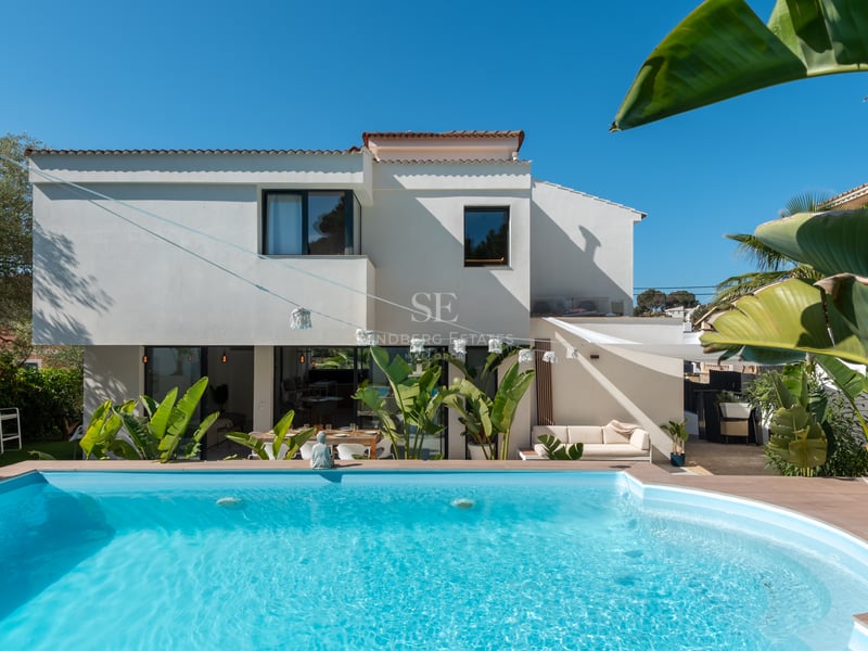 Piscine turquoise devant une villa contemporaine blanche entourée de palmiers sous un ciel bleu azur.
