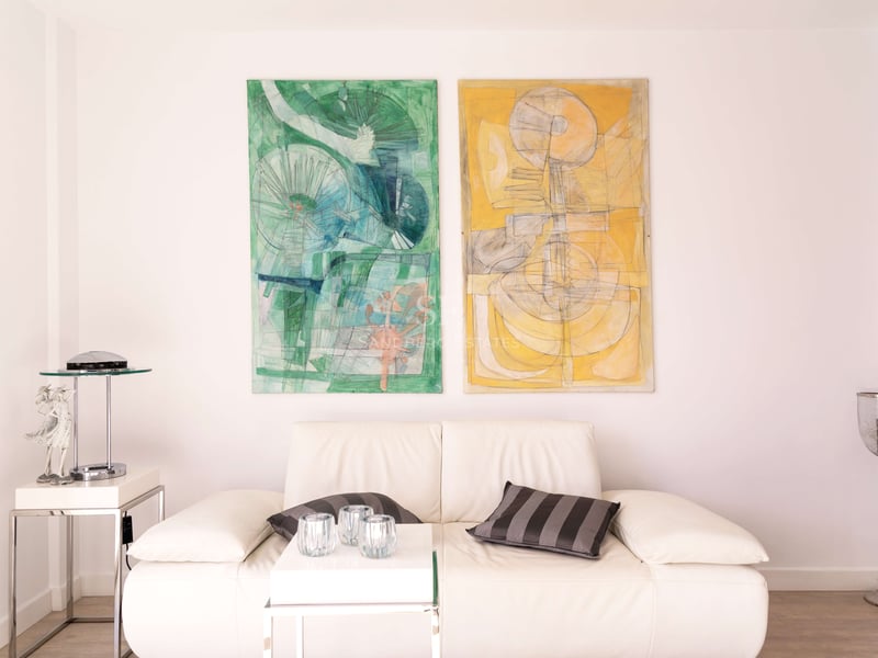 Canapé en cuir blanc avec finitions chromées et deux grandes peintures abstraites verte et jaune sur mur blanc.