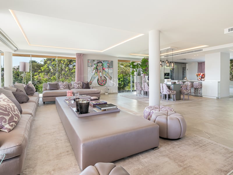 Vaste salon ouvert avec sol en marbre, accents roses, mobilier moderne et grandes baies vitrées sur le jardin.