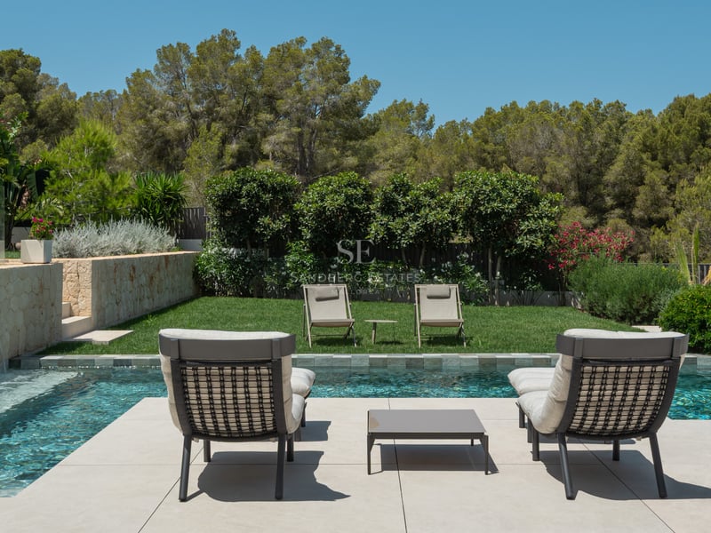 Espace piscine avec bains de soleil modernes, pelouse soignée et mur en pierre avec cascade sous un ciel bleu.