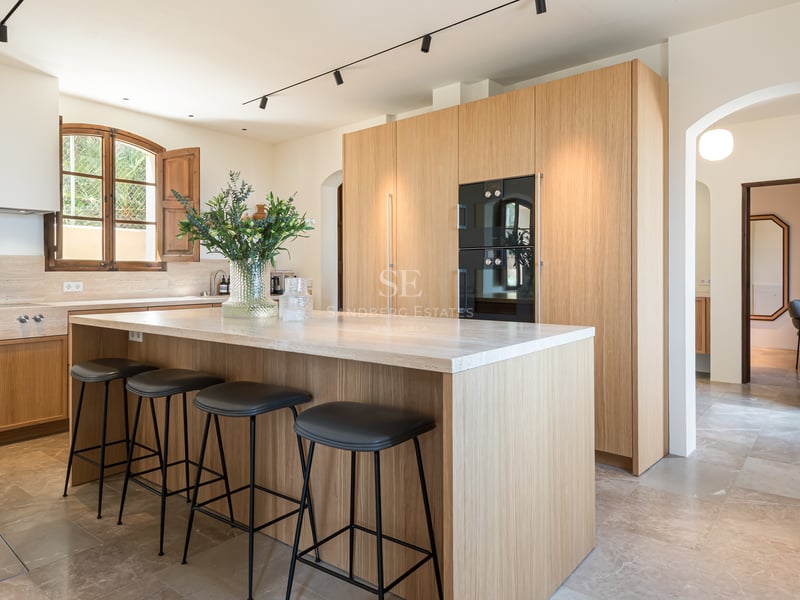 Cuisine contemporaine avec meubles en chêne, îlot en pierre naturelle, tabourets noirs et sol en marbre.