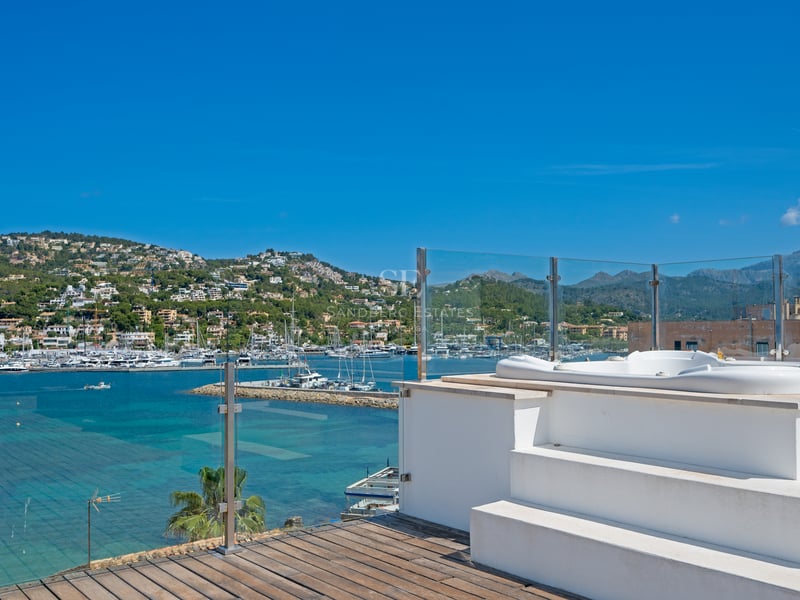 Terrasse sur le toit avec jacuzzi blanc, garde-corps en verre et vue panoramique sur le port de plaisance.