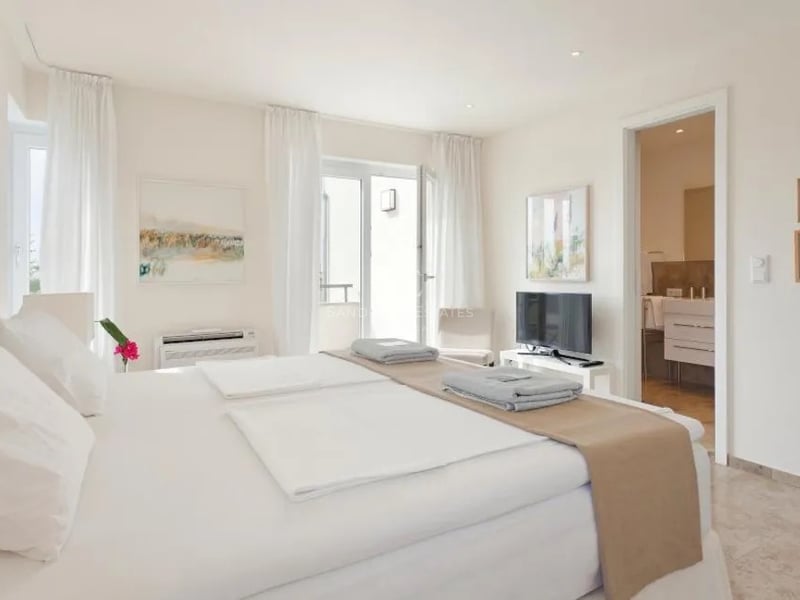 Chambre principale moderne blanche avec salle de bain attenante, sol en marbre et accès terrasse.