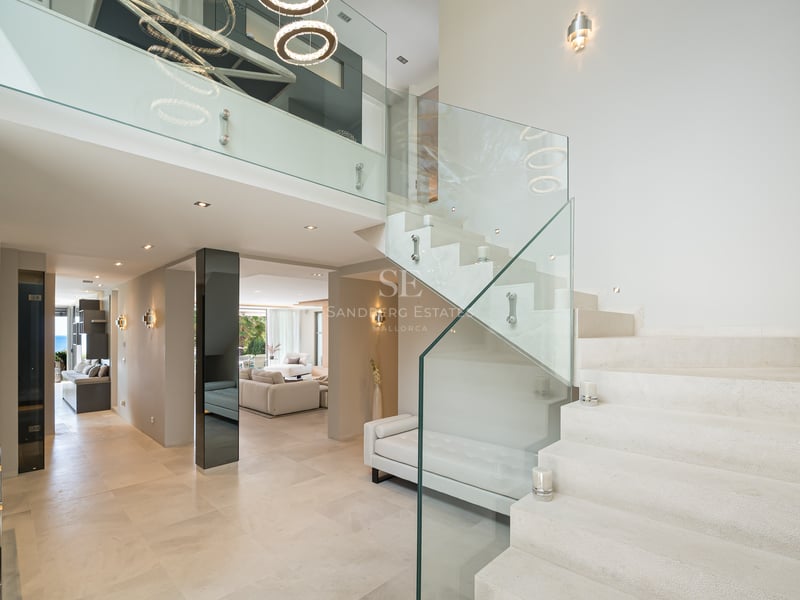 Entrée de villa moderne avec escalier en pierre, balustrades en verre et plafonds à double hauteur.