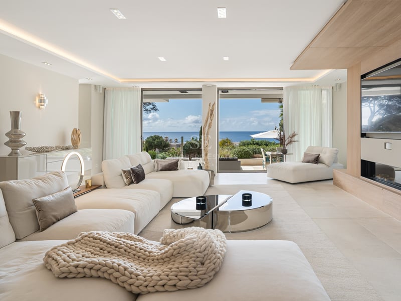Salon moderne avec canapés blancs, accents en chêne et grandes baies vitrées donnant sur la Méditerranée.