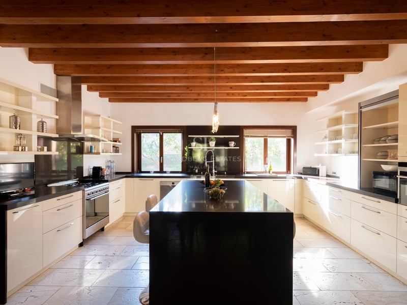 Grande cuisine moderne avec placards blancs, îlot en granit noir et plafond à poutres de bois traditionnelles.