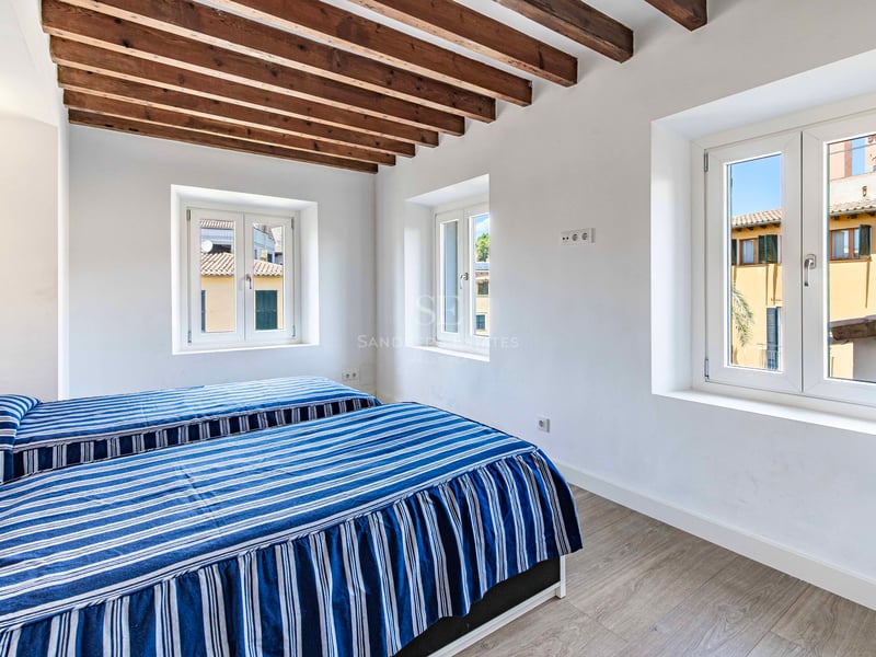 Chambre lumineuse avec deux lits simples, plafond à poutres en bois et fenêtres donnant sur la vieille ville.