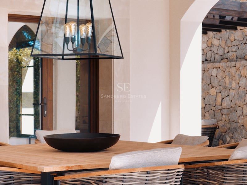 Table à manger en bois et chaises tressées sur une terrasse de luxe avec mur en pierre et lanterne design.