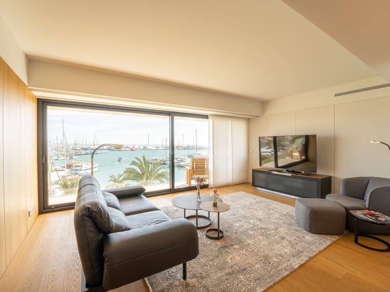 Salon contemporain avec canapé en cuir et grandes baies vitrées donnant sur un port avec des bateaux.