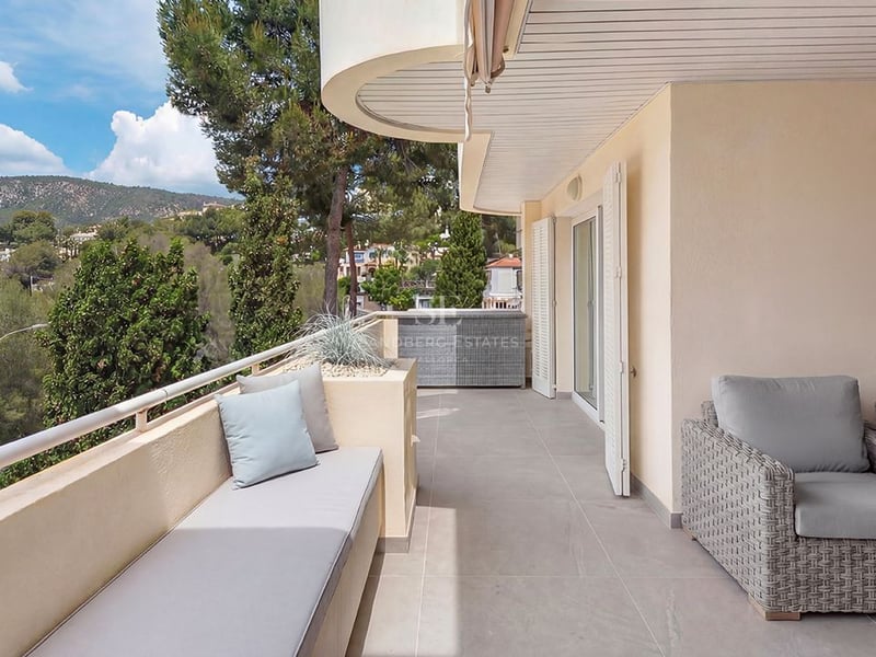 Terrasse couverte moderne avec meubles en rotin gris, banquette intégrée et vue sur les collines verdoyantes.