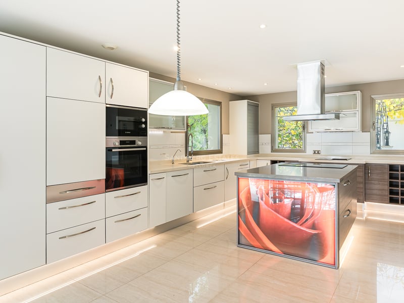 Cuisine blanche moderne avec électroménager en inox et un îlot central rétroéclairé affichant une rose orange.