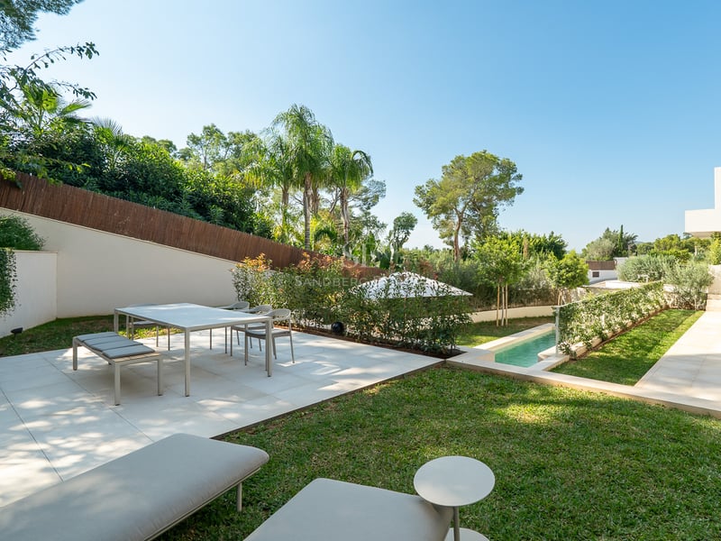 Terrasse moderne avec coin repas, barbecue et piscine entourée d'une végétation luxuriante et de palmiers.