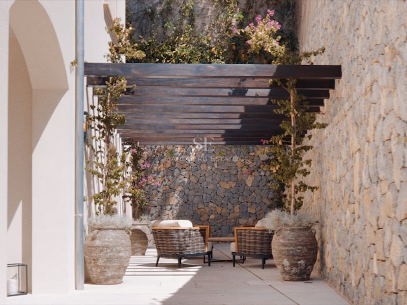 Terrasse méditerranéenne ensoleillée avec murs en pierre rustique, pergola en bois sombre et sièges extérieurs confortables.