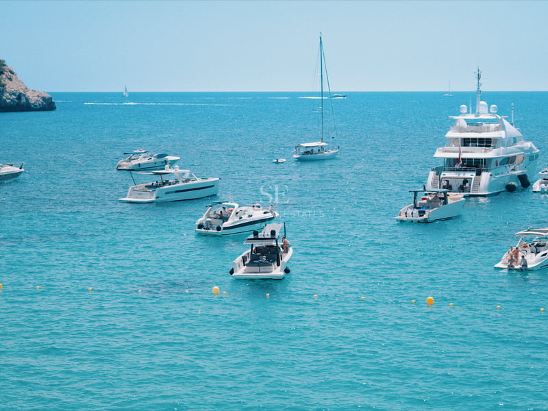 Plusieurs yachts de luxe et bateaux à moteur ancrés dans une baie aux eaux turquoise cristallines près de falaises.