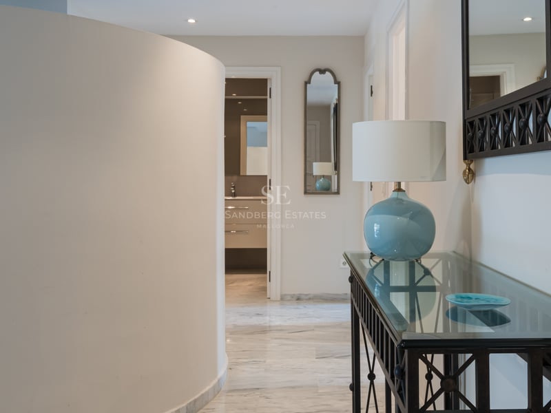 Entrée moderne avec mur incurvé, sols en marbre poli et console en verre avec lampe bleue.