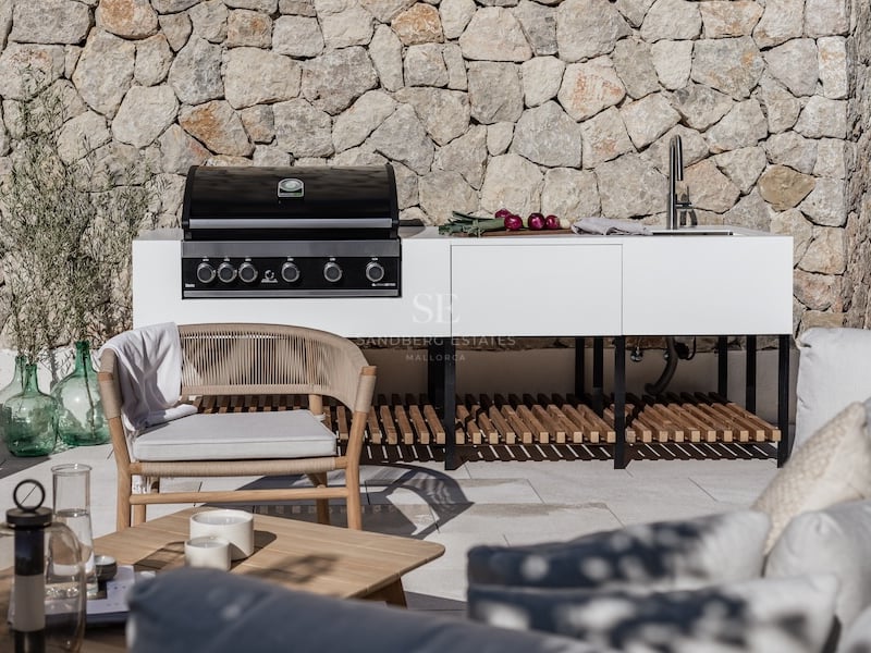 Cuisine extérieure moderne blanche avec barbecue et évier devant un mur en pierre naturelle et mobilier design.