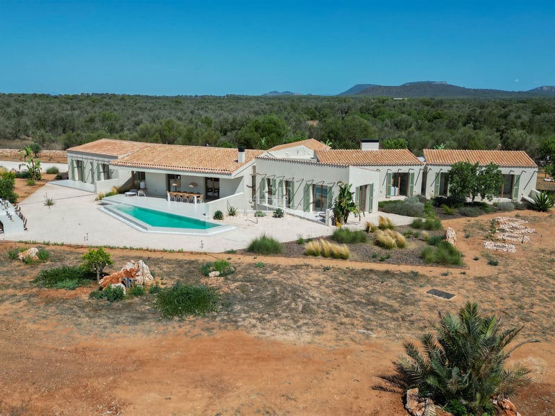 Aerial view of a modern single-story villa with terracotta roofs, geometric pool, and expansive natural landscape.