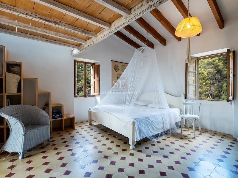 Chambre avec murs blancs, poutres en bois, sol en carrelage à motifs et lit avec moustiquaire.