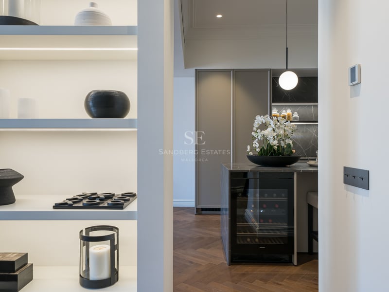 View of a modern kitchen island with built-in wine fridge, dark marble top, and herringbone wood floors.