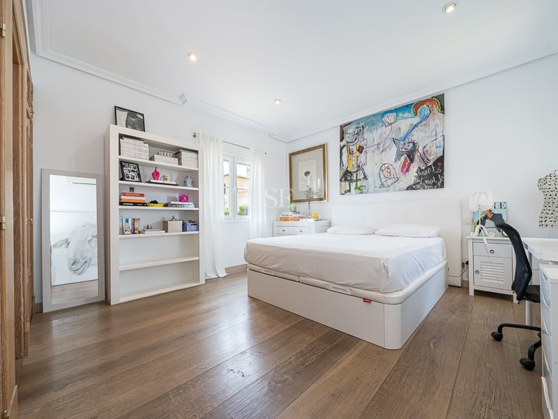 Chambre lumineuse avec murs blancs, parquet en bois, lit double, bibliothèque blanche et bureau.