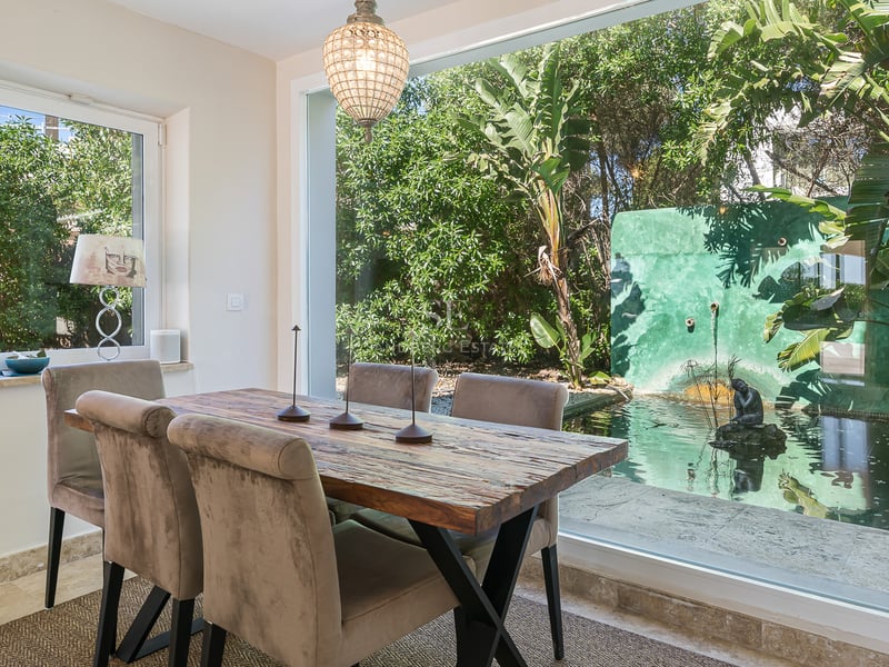 Salle à manger contemporaine avec table en bois rustique donnant sur un jardin avec bassin d'eau.