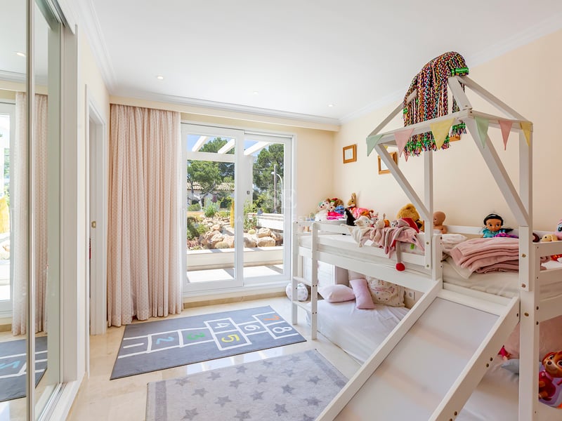 Chambre d'enfant avec lits superposés blancs et toboggan, sol en marbre et baies vitrées ouvrant sur le jardin.