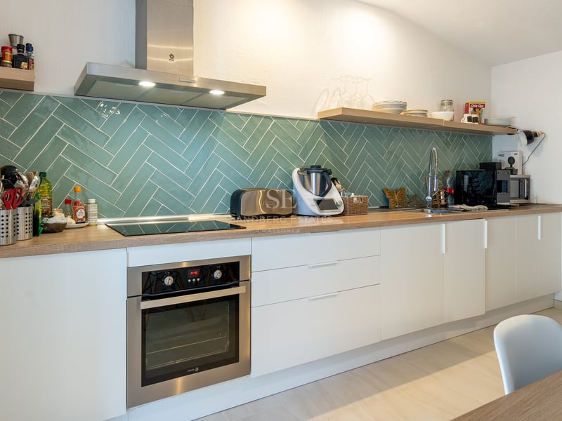Cuisine blanche moderne avec crédence en carrelage à chevrons bleu canard, plans de travail en bois et appareils inox.