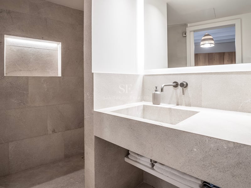 Salle de bain moderne avec lavabo en pierre intégré, miroir rétroéclairé et douche avec niche lumineuse.