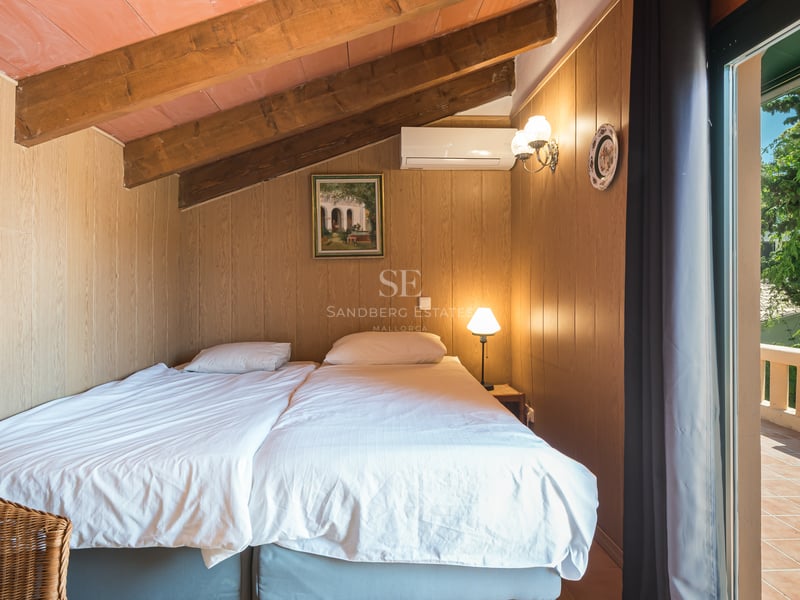 Chambre mansardée avec poutres apparentes, murs en bois et porte vitrée ouvrant sur une terrasse en terre cuite.