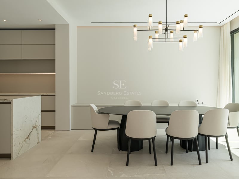 Salle à manger minimaliste avec table noire, chaises crème, îlot en marbre et baie vitrée donnant sur le jardin.