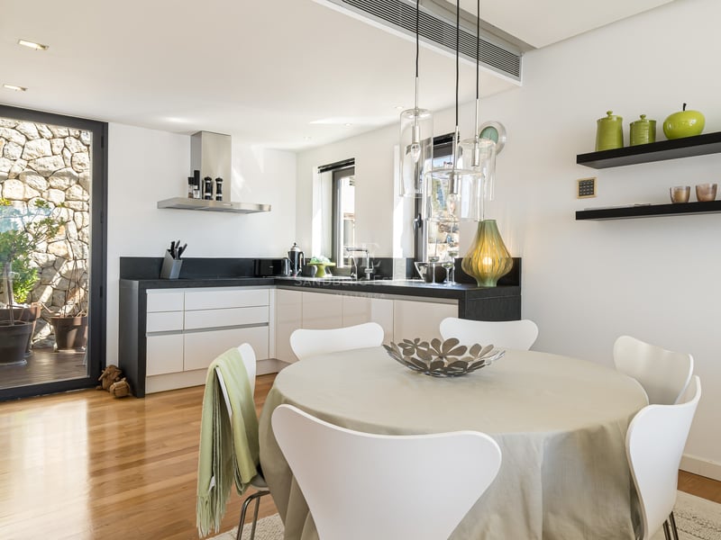 Cuisine lumineuse avec placards blancs, plans de travail noirs, parquet et table à manger ronde.