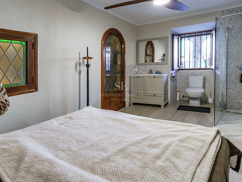 Chambre avec portes en bois et vitraux comprenant une salle de bain ouverte avec douche aux murs en galets.