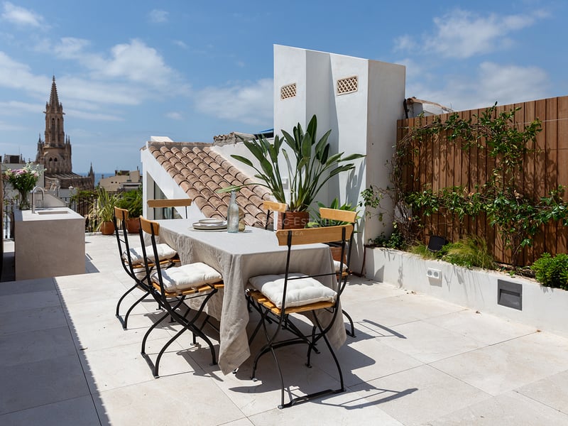 Terraza en la azotea con mesa de comedor, cocina exterior y vistas a la catedral gótica de Palma de Mallorca.