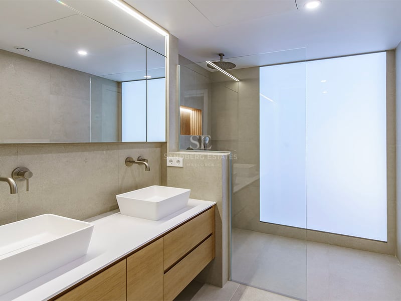 Baño moderno con lavabo doble de madera, lavabos blancos y ducha a ras de suelo con cristal translúcido.